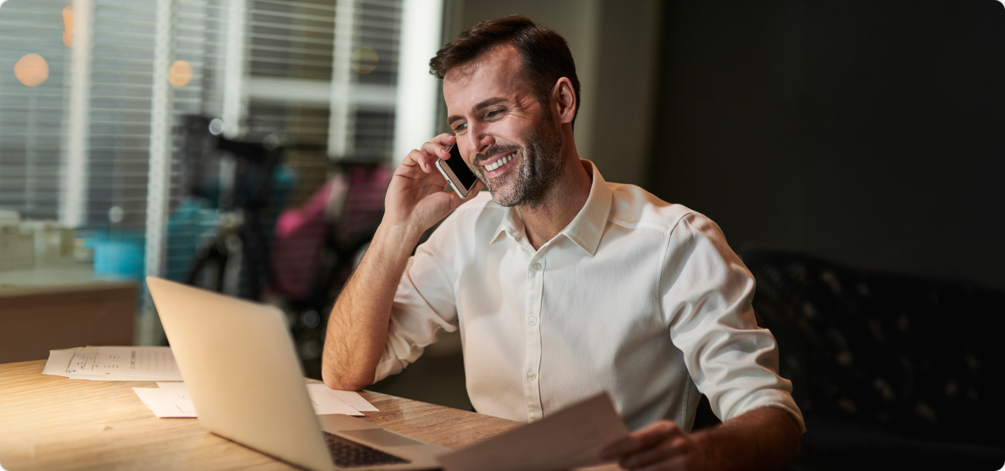 homem sorrindo em frente ao notebook enquanto fala no celular